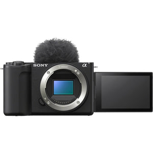 Fotocamera Sony ZV-E10 II nera solo corpo vista di fronte, senza obiettivo: l'innesto Sony E aperto con il sensore APS-C in vista, il paravento peloso montato sulla slitta e lo schermo aperto lateralmente