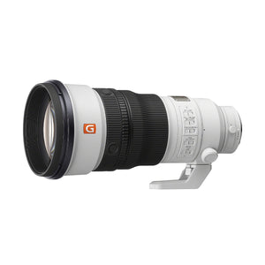 Super teleobiettivo Sony FE 300mm f/2.8 GM OSS di tre quarti dal davanti, barilotto bianco con il logo arancione G Master, il paraluce montato, il pannello degli interruttori e il piede per treppiede