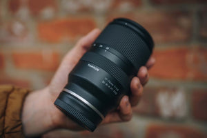 Tamron 17-70mm f/2.8 tenuto in mano davanti a un muro di mattoni