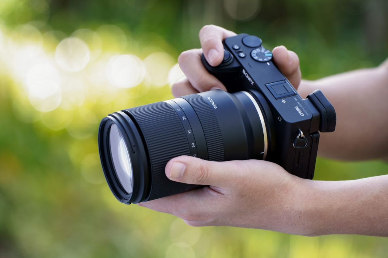 Tamron 17-70mm f/2.8 montato su fotocamera Sony impugnata a due mani, sfondo verde sfocato